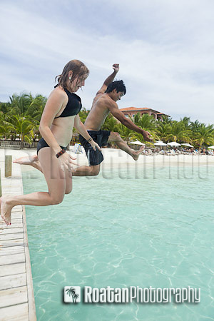 Couple jumping off dock into tropical sea