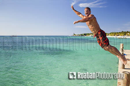 Man jumping off pier into caribbean sea stock photo